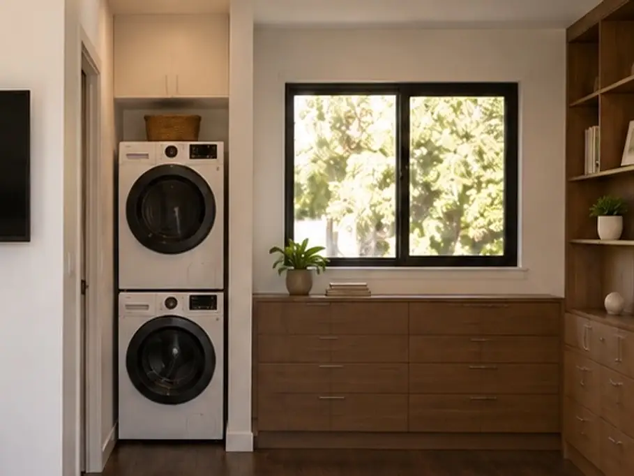 Detail of the rendering from the ADU 256 front door: the bath door, the stacked washer and dryer with a basket on top, and a walnut chest of drawers under the window.
